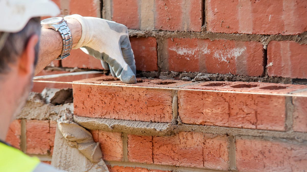 A construction worker places a brick precisely in a wall, ensuring stability and alignment.