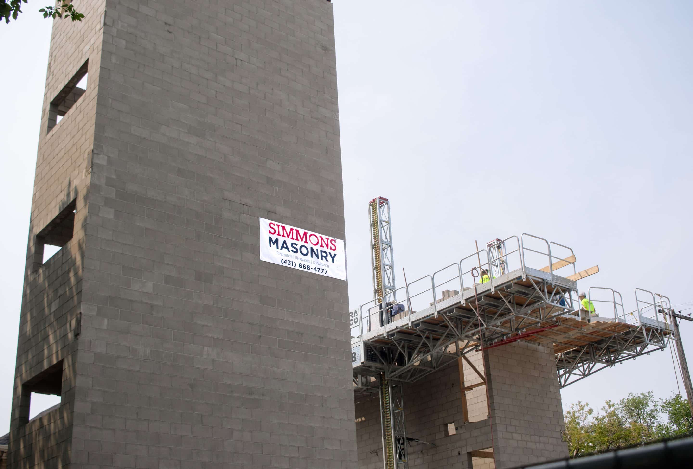 Scaffolding surrounds the construction zone, providing support and access to higher sections of the wall. The environment is typical of an active construction site, with workers focused on their tasks to erect a new building.